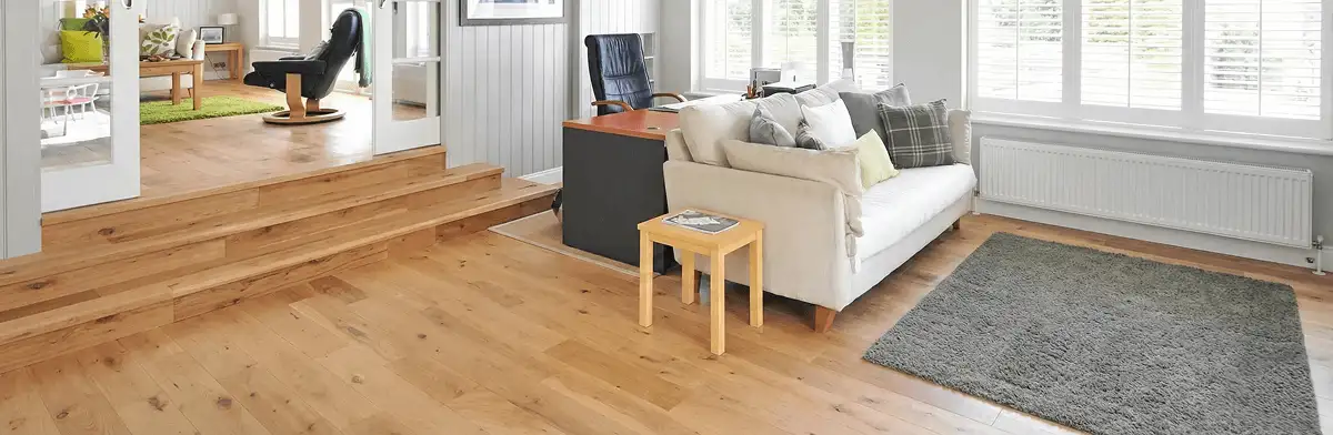 A modern living room with professionally installed laminate flooring, a beige sofa, a small side table, a gray rug, and large windows with white shutters in Norfolk, VA